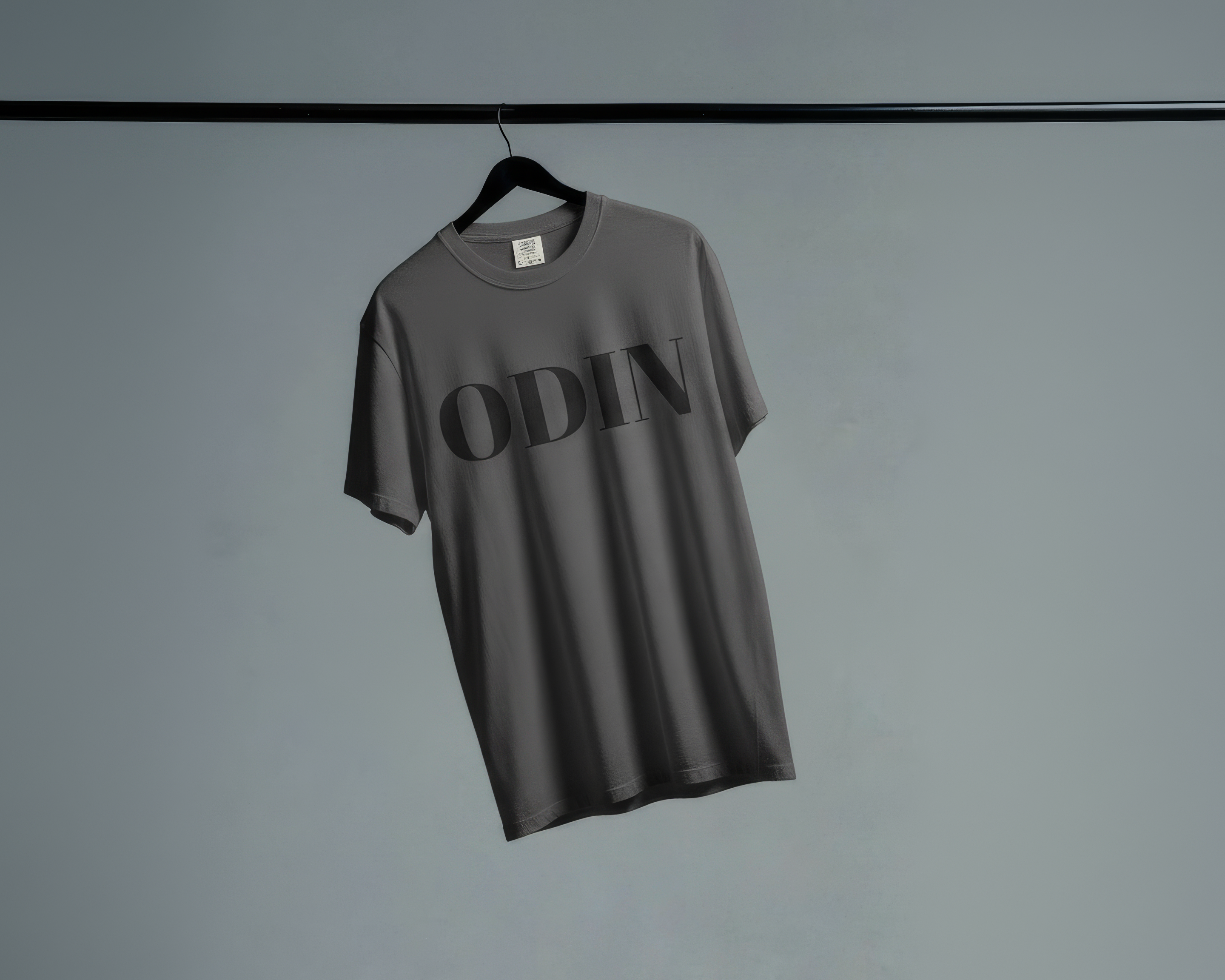 Gray t-shirt with 'ODIN' branding on a hanger against a plain background